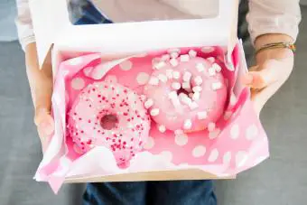 Chica sujetando caja con donuts, vista parcial 