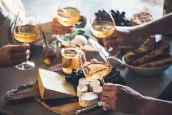 Manos de personas sosteniendo copas de vino en la mesa de quesos
