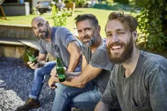 Amigos felices sentados con botellas de cerveza en el jardín