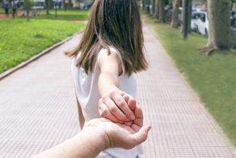 Una escena detrás de una niña sosteniendo la mano de su padre.