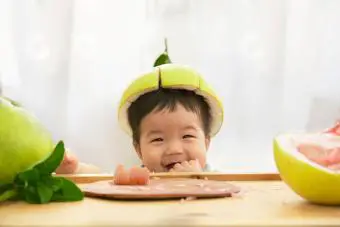 Niño comiendo fruta, luciendo tonto con piel de pomelo como sombrero