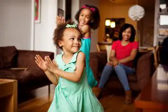 Madre viendo hijas felices bailando en la sala de estar 