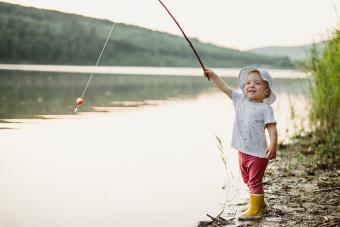 Niña sosteniendo una caña de pescar junto a un lago