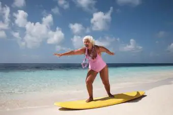 Anciana de pie sobre una tabla de surf en la playa.