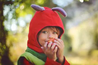 Niño disfrazado de oruga comiendo una manzana.