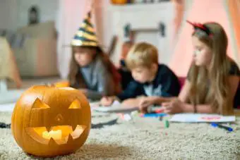 Linterna de Halloween con velas en la alfombra de peluche, niños dibujando en segundo plano.