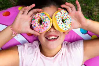 Chica divertida usando donuts coloridos como vasos