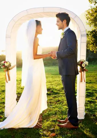 La novia y el novio parados frente al arco de la boda