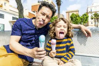 Feliz padre e hijo sentados en el banco disfrutando de un helado