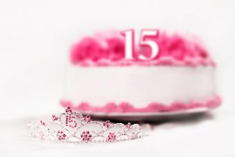 Una tiara usada por una niña que celebra su cumpleaños número 15 se muestra frente a un pastel de cumpleaños.