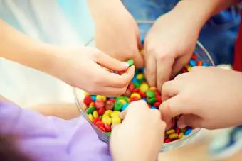 Manos de niños sacando coloridos dulces de chocolate de un bol