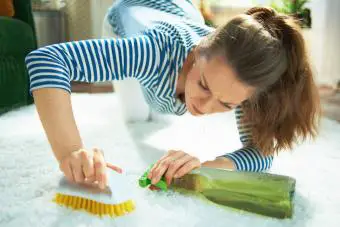 Mujer con agente de limpieza y cepillo limpiando la alfombra