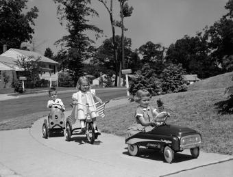 Niños de la década de 1950 montando autos y bicicletas de juguete en la acera