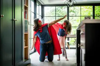Chica con madre en traje de superhéroe rojo en casa