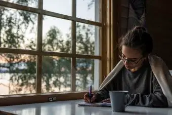 Mujer sentada junto a la ventana escribiendo en el diario