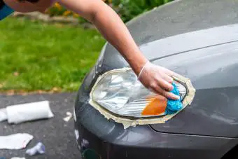 Hombre limpiando los faros de los coches pegados para proteger el roce de la pintura con una toalla azul