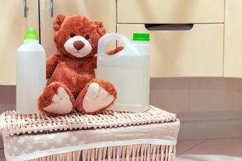 Un oso de peluche se sienta en una canasta de ropa en el baño junto al detergente y el abrillantador