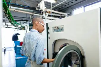 Mujer joven poniendo ropa en una máquina de limpieza en seco