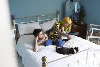 Una joven pareja hipster acostada en su cama jugando con su gato mascota 