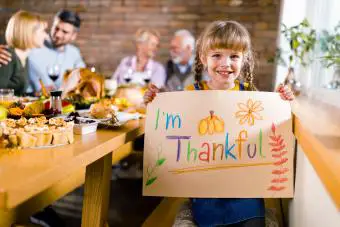 Chica feliz con cartel durante la comida de Acción de Gracias con sus padres y abuelos