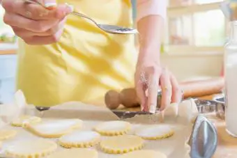 mujer rociando azúcar en masa para galletas en la cocina