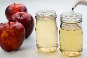 Sirviendo vinagre de sidra de manzana en botellas de vidrio con manzanas rojas en el fondo.