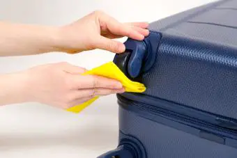 Limpiar las ruedas de goma de una maleta de viaje con un paño amarillo