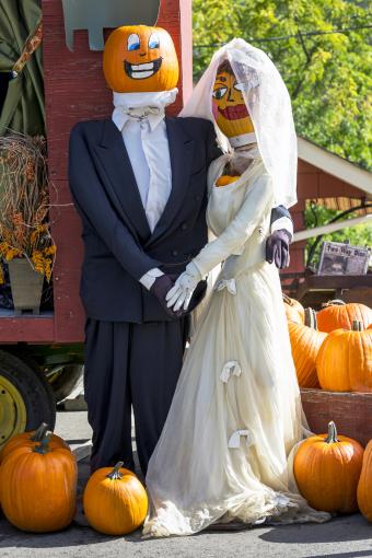 Maniquíes vestidos como una pareja casada con cabezas de calabaza pintadas rodeadas de calabazas