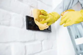 Mujer con guantes protectores desinfectando interruptores de pared mientras limpia en casa