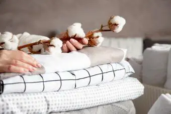 Manos de mujer sosteniendo una rama de algodón con un montón de sábanas y mantas dobladas
