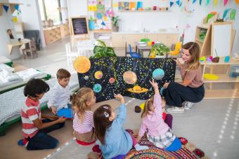 Un maestro mostrando un cartel con planetas a los niños.