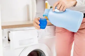 Manos femeninas vertiendo detergente en la tapa de la botella 