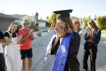Mujer joven vestida con un sombrero de graduación rodeada de sus amigos y familiares 