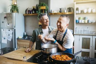 Feliz pareja gay de mediana edad cocinando en la cocina