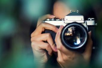 Mujer fotógrafa disparando con una cámara analógica entre hojas de árboles al atardecer 