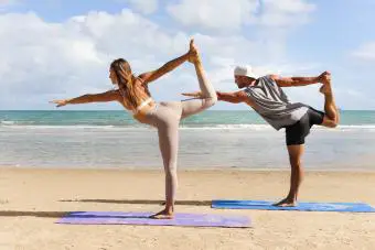 mujer, hombre haciendo yoga y estirando el cuerpo en la playa de la isla de verano
